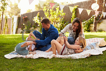 Parents Playing Game With Children On Blanket In Garden