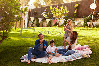Parents Blowing Bubbles With Children On Blanket In Garden