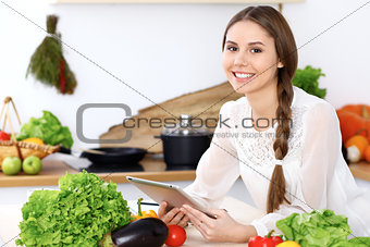 Young  happy woman is making online shopping by tablet computer while smiling. Housewife looking for a new recipe for  cooking in a kitchen