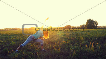 Beautiful young brunette woman doing yoga exercise on the field during amazing sunset.