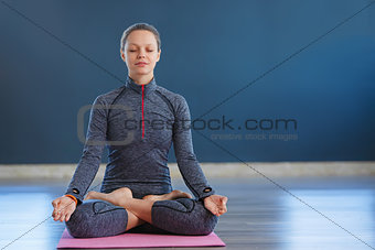 Beautiful young woman sitting in Lotos pose. woman practicing meditation in yoga hall after hard day.