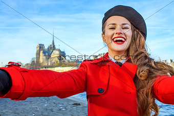 smiling woman on embankment in Paris, France taking selfie