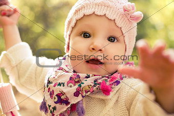 Closeup portrait of beautiful baby girl wearing stylish hat and cozy sweater. Outdoors spring, autumn photo.