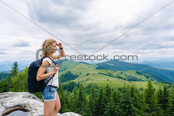 A young girl stands on top of a mountain in cloudy weather enjoying the view