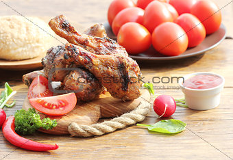 Grilled chicken legs with vegetables on cutting board.