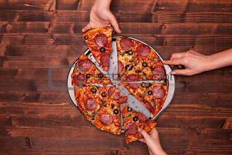 Hands taking pizza slices off the baking pan