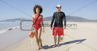 Female and male lifeguards walking along beach