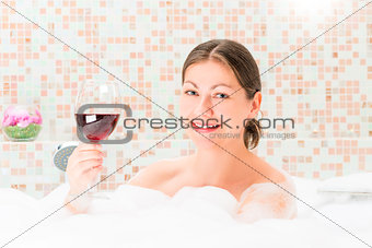 portrait of a happy girl in a bath with a glass of drink