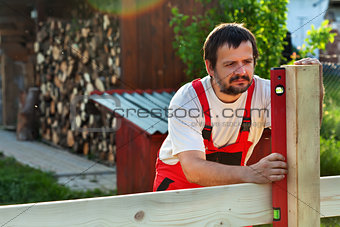 Man building a wooden fence - checking the posts with a level