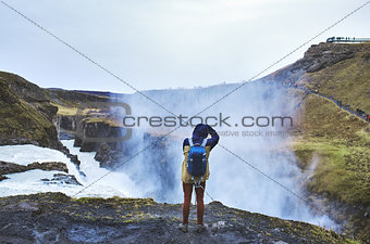 A man stands on the edge of a waterfall Gullfoss and takes pictures of him