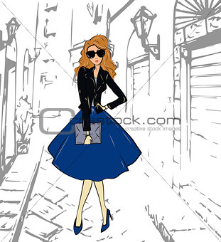 Fashionable cute girl in a leather jacket, blue midi skirt and shoess walking down the street
