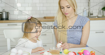 Cheerful girl painting eggs with mother