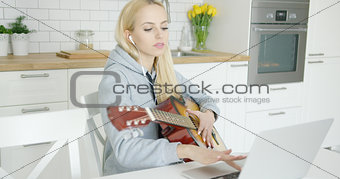 Girl practicing guitar and using laptop