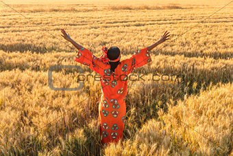 African woman in traditional clothes arms raised in field of cro