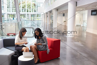 Two Businesswomen Using Mobile Phones In Lobby Of Office