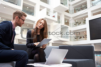 Two Businesspeople Using Laptop In Lobby Of Modern Office