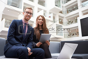 Two Businesspeople Using Laptop In Lobby Of Modern Office