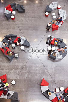 Students groups sit in a modern university atrium, vertical