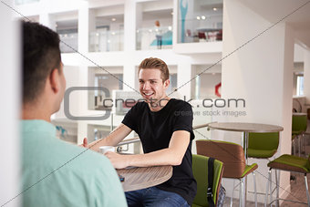 Young adult male students talking in modern university cafe