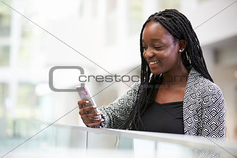 Young black female student using phone in university foyer