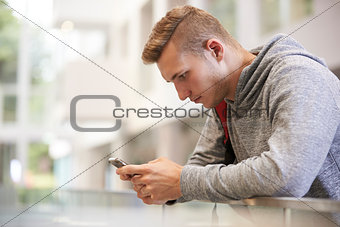 Young adult male student uses smartphone in university lobby