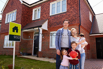 Portrait Of Family Outside New Home With Sold Sign