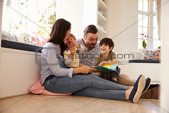 Family Sitting On Floor Reading Story At Home Together