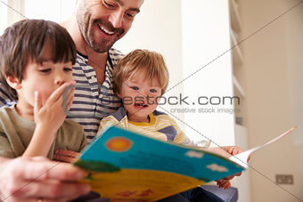Close Up Of Father And Sons Reading Story At Home Together