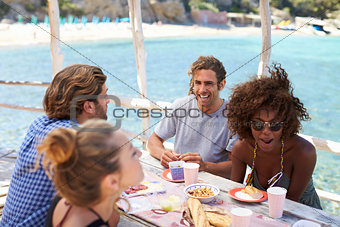 Two female friends talking over drinks at a table by the sea