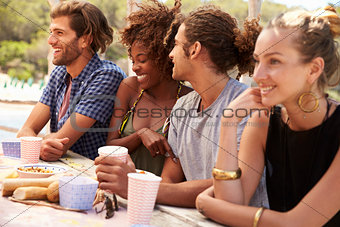 Four friends sit in a row at a table by the sea, close up