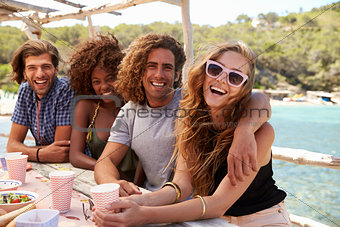 Two couples sitting at a table by the sea look at each other