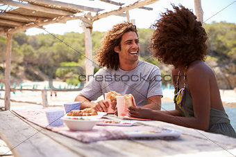 Young couple sit at a table by the sea looking at each other