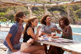 Two couples relaxing at a table by the sea, look to camera