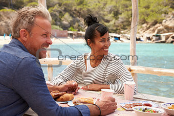 Middle aged couple at table by the sea looking at each other