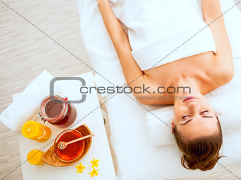 Young woman laying on massage table near honey spa therapy ingre