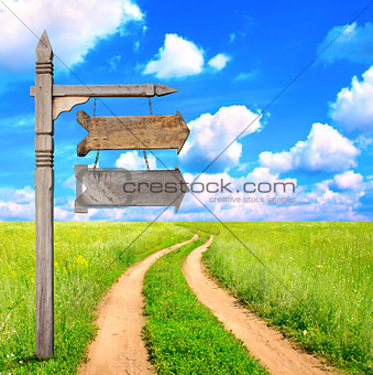Rural summer landscape with dirt road and old wooden signboard 