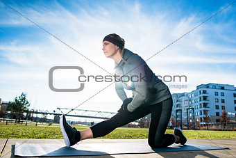 Determined young woman stretching her leg while kneeling on a ma