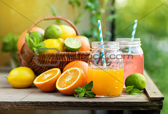 Mix of fresh citrus fruits in basket and juice in glass jars.