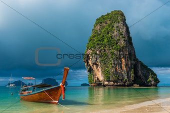 Traditional wooden Thai boat near the shore and high cliff