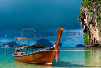 A Thai boat with a long tail near the shore, a blue rain cloud o