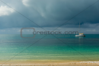 A gloomy sky above the turquoise calm sea and a small white yach