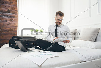 Businessman on bed working with a tablet and laptop from his hotel room
