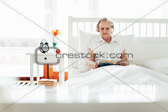 Elderly woman sitting comfortably in bed reading her favourite book