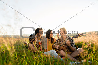 Young people sitting together in grass playing guitar