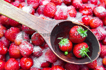 Against a background of strawberries with sugar a wooden spoon for jam.