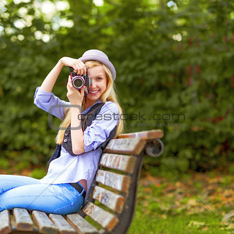 Young hipster taking photo with retro photo camera sitting on be