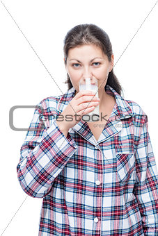 Woman in plaid pajamas drinks milk before bed on a white backgro