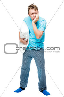 Sleepy man in pajamas with a pillow in his hand on a white backg