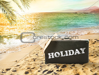Suitcase in a tropical beach with holiday writing