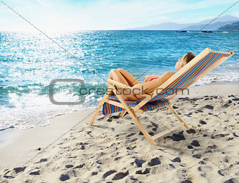 Girl tans on a deck chair on a beautiful beach